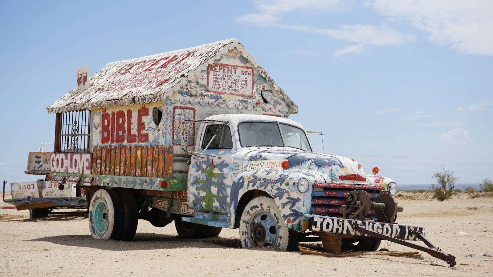 20 American Disaster Towns Forever Marked by One Terrifying Day 19 A vibrant, graffiti-covered truck displaying religious messages in Slab City, California desert.